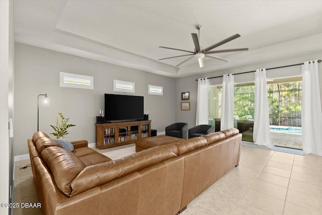 living room with a raised ceiling, ceiling fan, and light tile patterned flooring