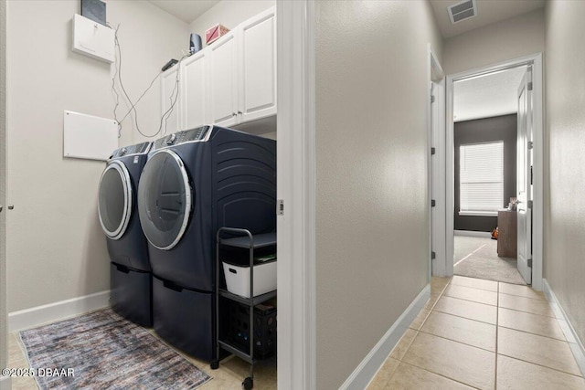 clothes washing area with cabinets, washing machine and dryer, and light tile patterned floors