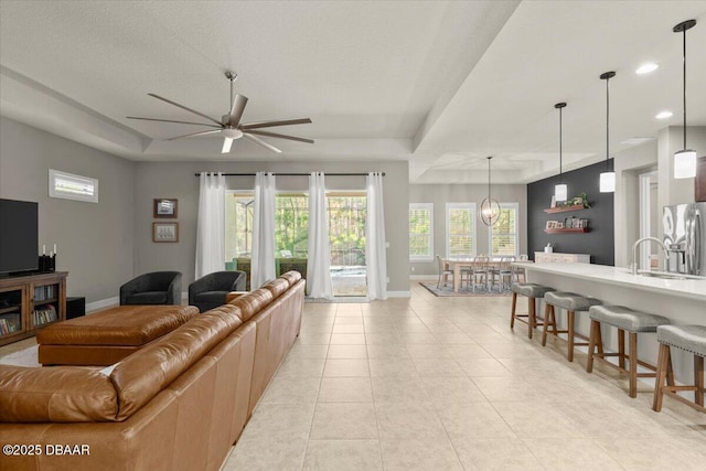 tiled living room featuring a textured ceiling, ceiling fan with notable chandelier, a raised ceiling, and sink