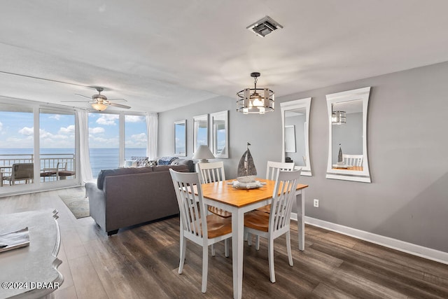 dining space featuring ceiling fan with notable chandelier, a water view, and dark wood-type flooring