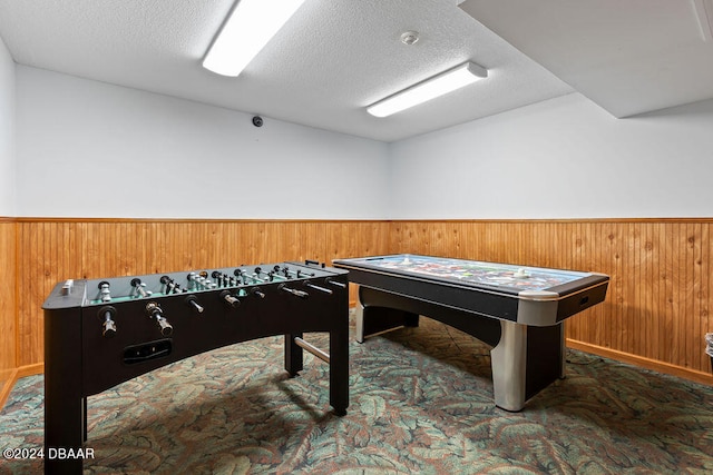 game room featuring wood walls, a textured ceiling, and dark colored carpet