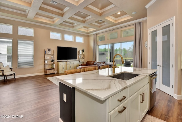 kitchen with light stone countertops, a kitchen island with sink, sink, hardwood / wood-style floors, and white cabinetry