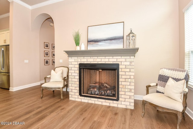 living area with a fireplace, wood-type flooring, and ornamental molding