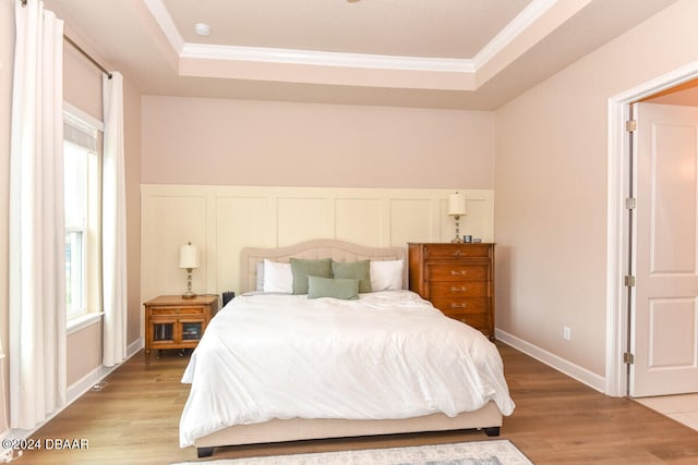 bedroom with light wood-type flooring, a raised ceiling, and crown molding