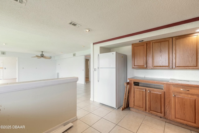 kitchen featuring visible vents, light countertops, brown cabinetry, and freestanding refrigerator