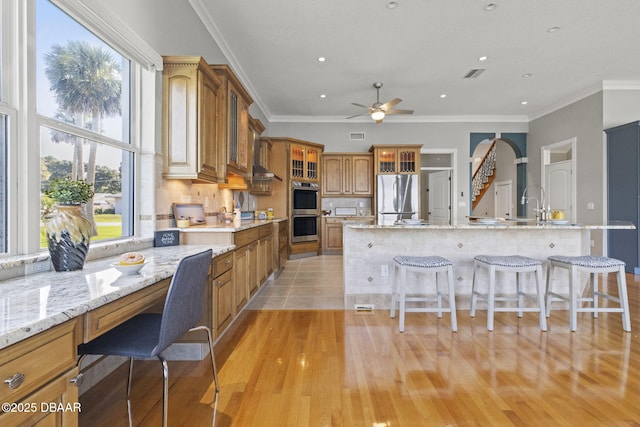 4210 S Peninsula Dr, Port Orange, FL 32127 - kitchen featuring appliances with stainless steel finishes, a kitchen breakfast bar, brown cabinetry, ceiling fan, and ornamental molding