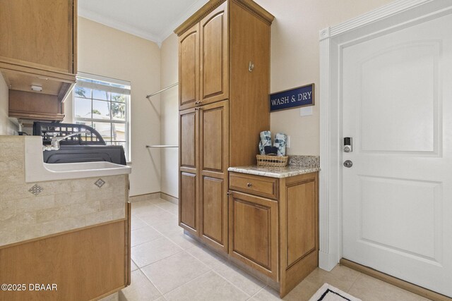 4210 S Peninsula Dr, Port Orange, FL 32127 - kitchen with ornamental molding, light tile patterned floors, brown cabinets, a sink, and baseboards