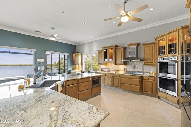 4210 S Peninsula Dr, Port Orange, FL 32127 - kitchen featuring wall chimney exhaust hood, appliances with stainless steel finishes, ceiling fan, a sink, and brown cabinets