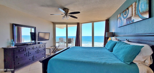 bedroom featuring ceiling fan, expansive windows, light tile patterned floors, a textured ceiling, and access to outside