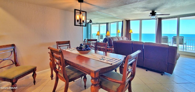 dining room with baseboards, light tile patterned flooring, a water view, a textured ceiling, and ceiling fan with notable chandelier