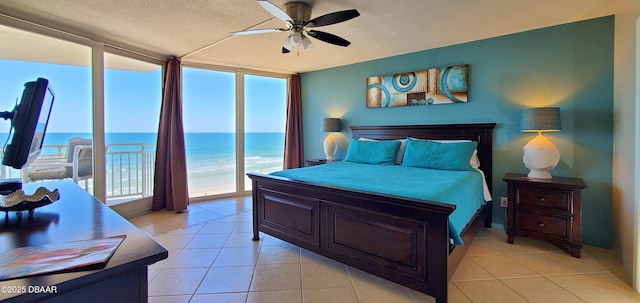 bedroom featuring light tile patterned floors, a ceiling fan, floor to ceiling windows, a water view, and a textured ceiling