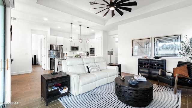 living room with ceiling fan, a raised ceiling, and wood-type flooring