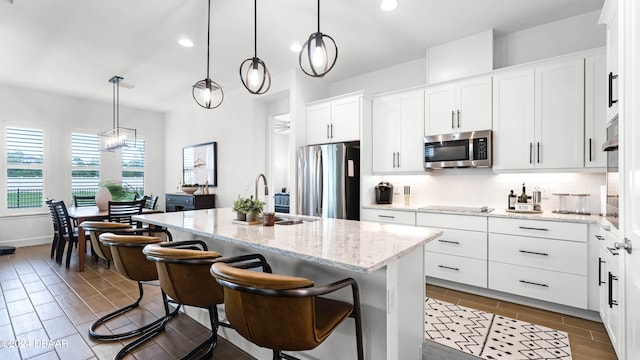 kitchen featuring white cabinetry, hanging light fixtures, an island with sink, a breakfast bar area, and appliances with stainless steel finishes