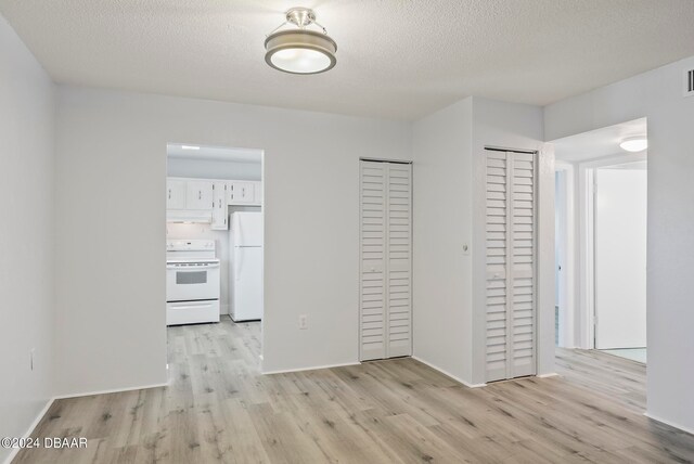 unfurnished bedroom with a textured ceiling, light hardwood / wood-style flooring, white fridge, and two closets