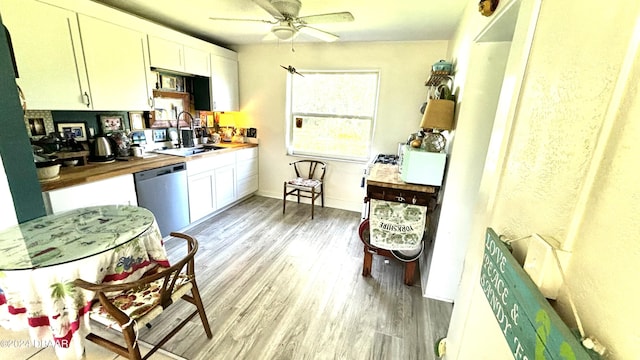 kitchen with wooden counters, light wood-type flooring, stainless steel dishwasher, sink, and white cabinetry