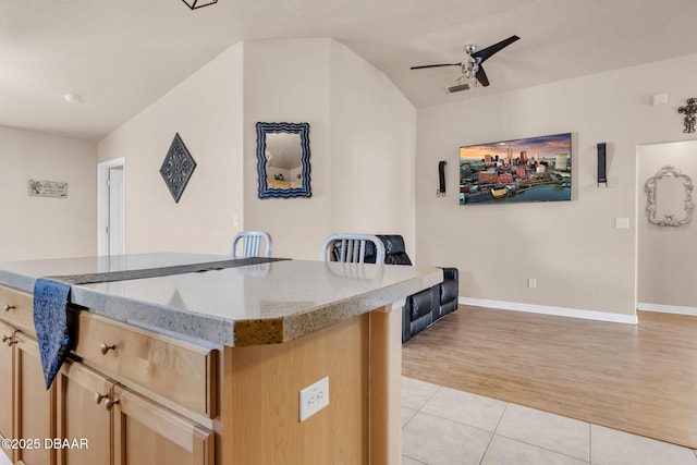 kitchen with a ceiling fan, light brown cabinetry, light stone counters, light tile patterned floors, and baseboards