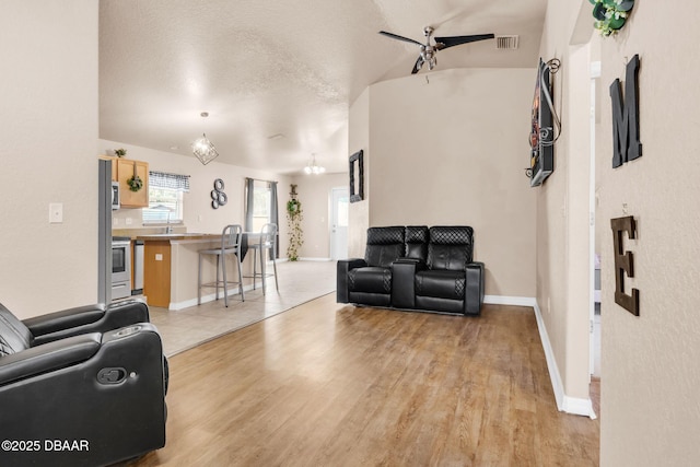 living room featuring visible vents, baseboards, light wood-style floors, and a textured ceiling