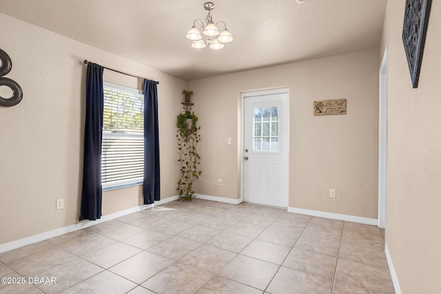 unfurnished room with light tile patterned floors, a notable chandelier, and baseboards