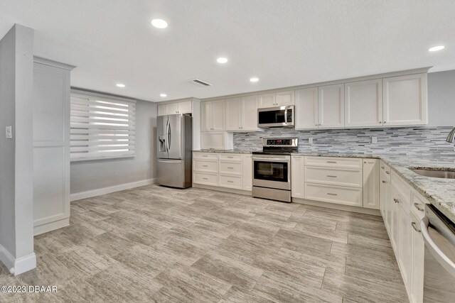 kitchen with stainless steel appliances, sink, tasteful backsplash, and light stone countertops