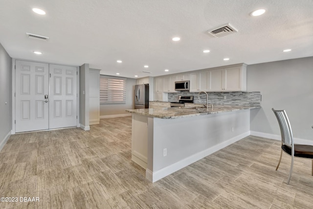 kitchen featuring stainless steel appliances, light wood-type flooring, light stone countertops, white cabinets, and kitchen peninsula