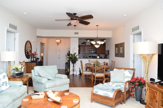 living room featuring ceiling fan with notable chandelier, visible vents, and light wood-style floors