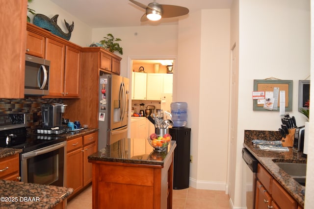 kitchen with light tile patterned floors, dark stone counters, brown cabinetry, backsplash, and appliances with stainless steel finishes