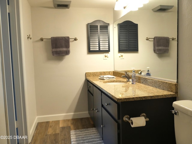 bathroom featuring vanity, toilet, baseboards, wood finished floors, and visible vents