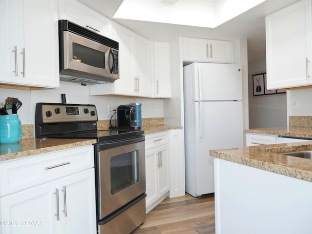 kitchen with light wood-type flooring, white cabinetry, light stone counters, and stainless steel appliances