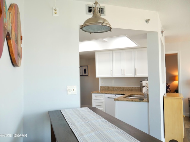 kitchen featuring white dishwasher, a sink, stone countertops, white cabinetry, and visible vents