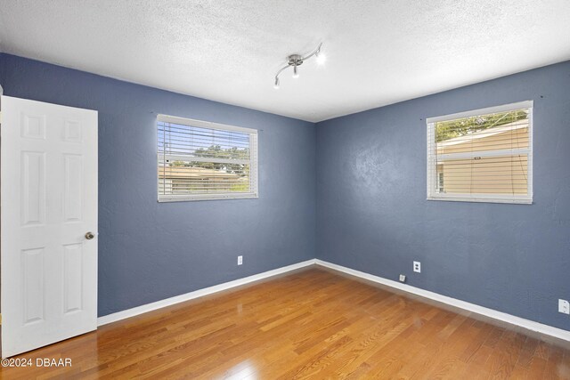 empty room with a textured ceiling, wood-type flooring, and a healthy amount of sunlight