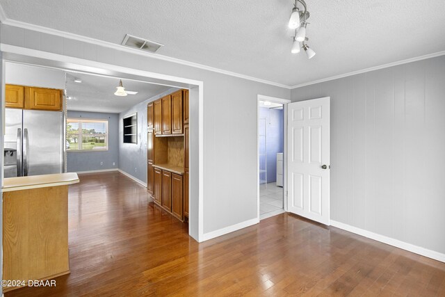 kitchen with stainless steel refrigerator with ice dispenser, a textured ceiling, light wood-type flooring, and ornamental molding