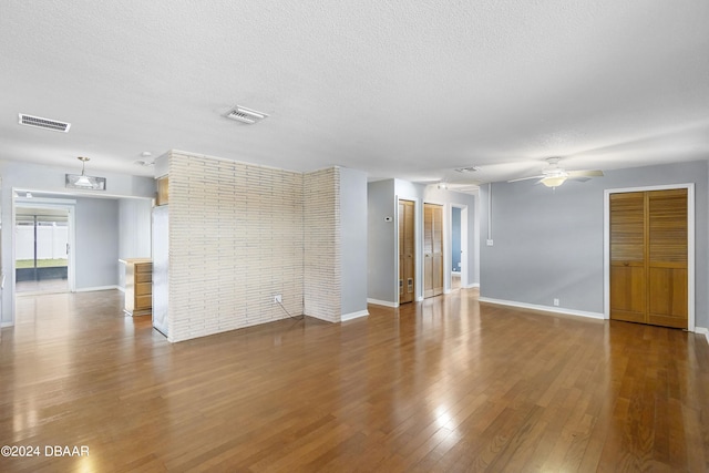 unfurnished room with ceiling fan, wood-type flooring, a textured ceiling, and brick wall