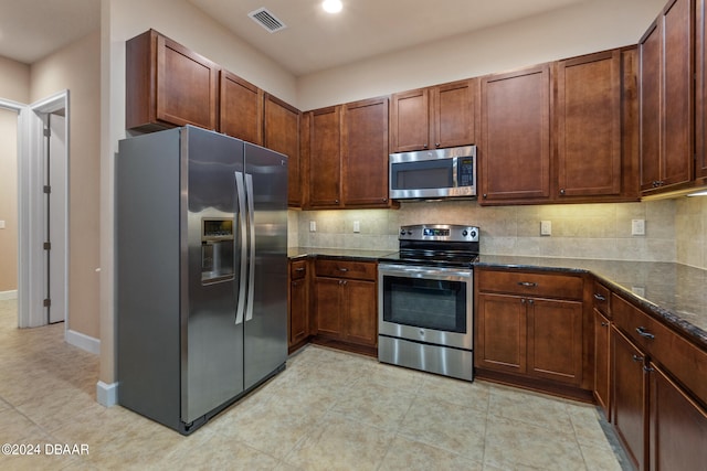 kitchen with stainless steel appliances, dark stone counters, light tile patterned floors, and backsplash