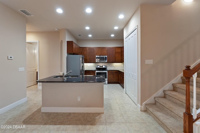 kitchen with stainless steel appliances, a center island with sink, sink, light tile patterned floors, and dark stone countertops