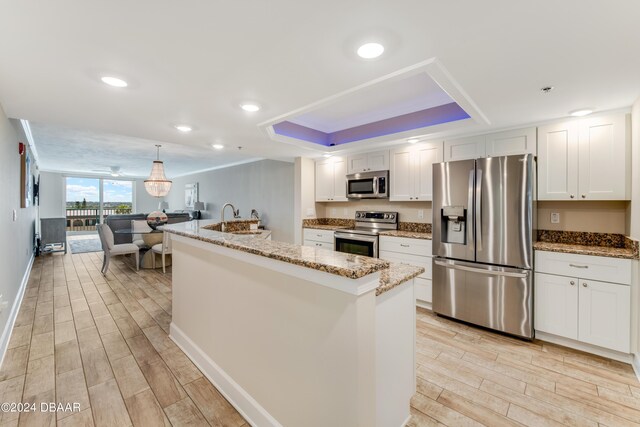 3797 S Atlantic Ave Unit 404, Daytona Beach, FL 32118 - kitchen featuring appliances with stainless steel finishes, wood finish floors, a raised ceiling, white cabinetry, and light stone counters