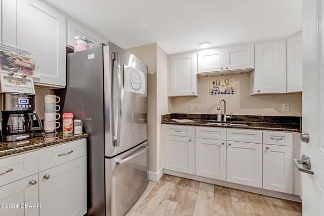 3797 S Atlantic Ave Unit 404, Daytona Beach, FL 32118 - kitchen with freestanding refrigerator, a sink, light wood-style flooring, white cabinetry, and dark stone counters
