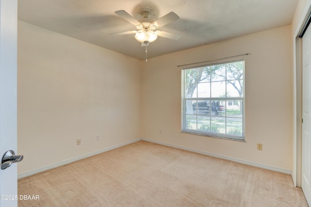 empty room featuring a ceiling fan, light colored carpet, and baseboards