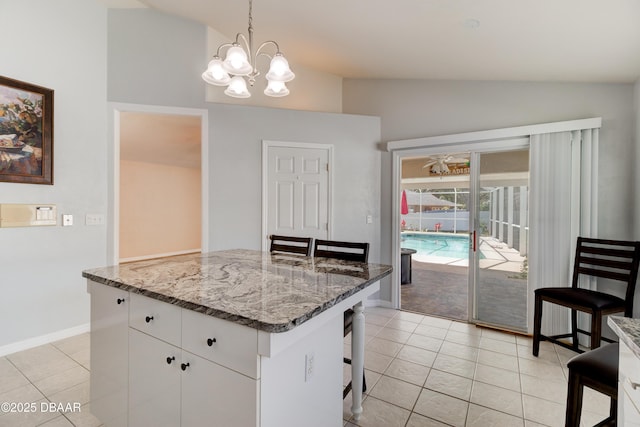 kitchen with light stone counters, pendant lighting, a breakfast bar area, white cabinets, and vaulted ceiling