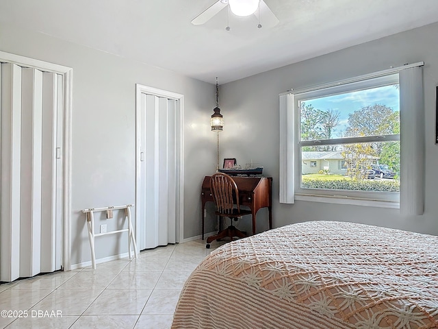 bedroom featuring light tile patterned floors, baseboards, a ceiling fan, and multiple closets