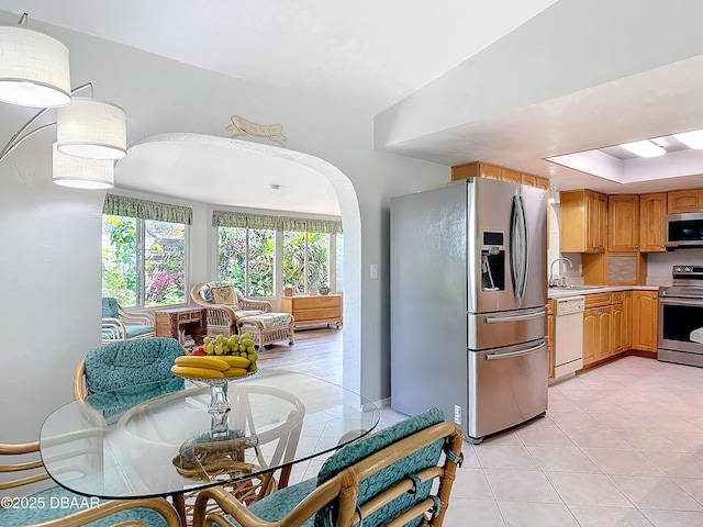 kitchen featuring arched walkways, light tile patterned floors, stainless steel appliances, light countertops, and a sink