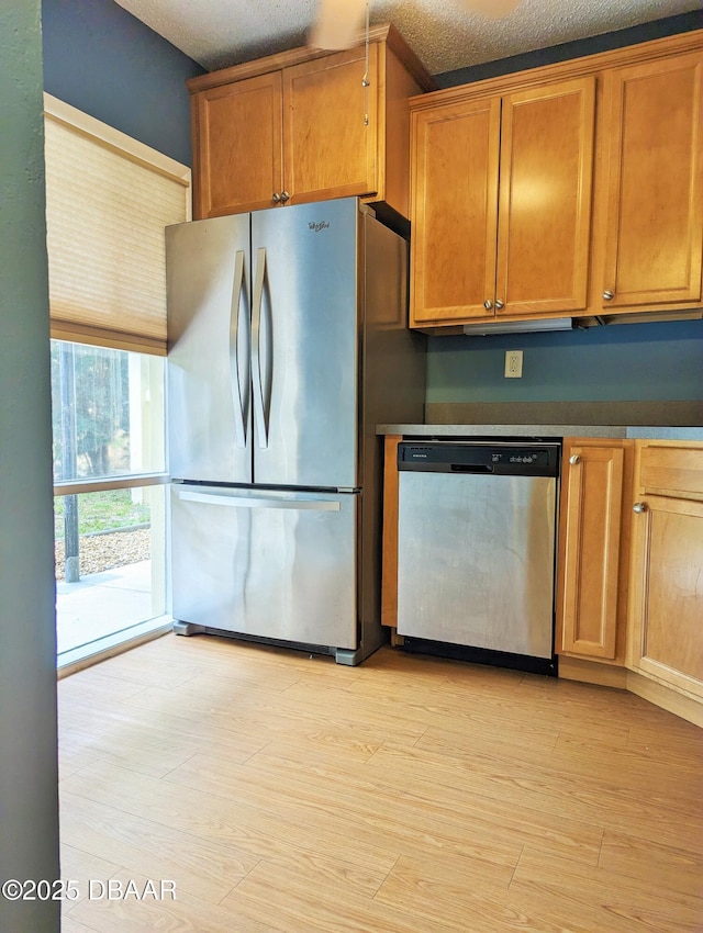 717 S Beach St Unit 102C, Daytona Beach, FL 32114 - kitchen with appliances with stainless steel finishes, brown cabinetry, light wood-style flooring, a textured ceiling, and dark countertops
