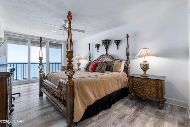 bedroom with a water view, access to outside, baseboards, and wood finished floors