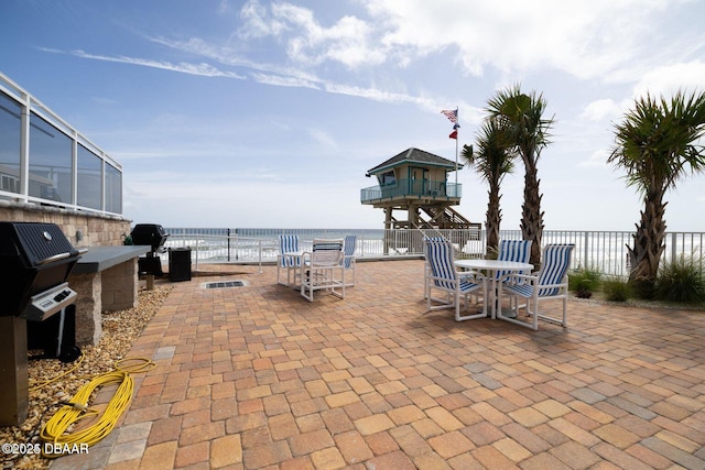 view of patio with exterior kitchen, a water view, and fence