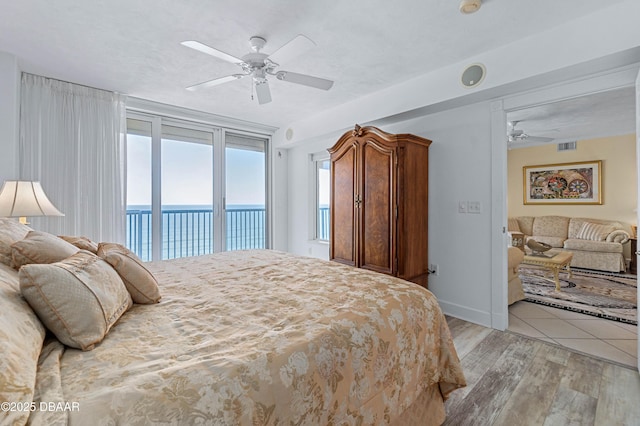 bedroom featuring access to exterior, visible vents, a water view, light wood-style flooring, and a ceiling fan