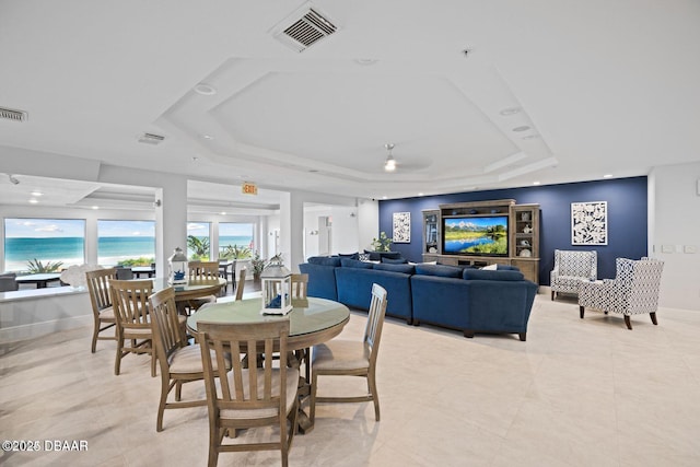 dining area with a raised ceiling, visible vents, a water view, and baseboards