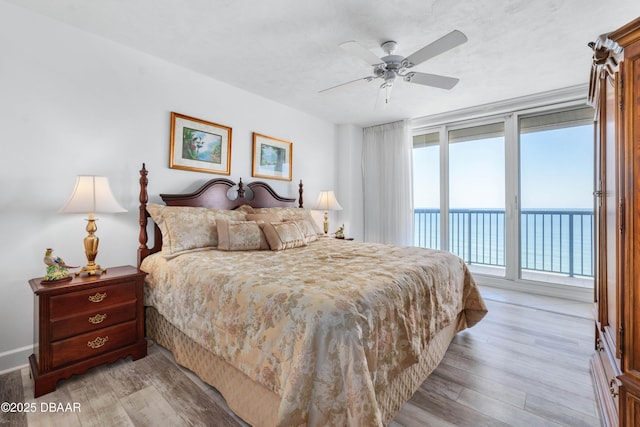 bedroom featuring access to exterior, light wood-type flooring, a water view, and ceiling fan