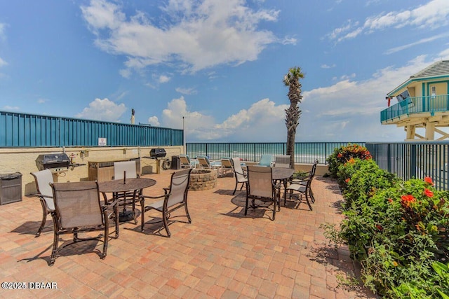 view of patio with a beach view, grilling area, a water view, fence, and outdoor dining space