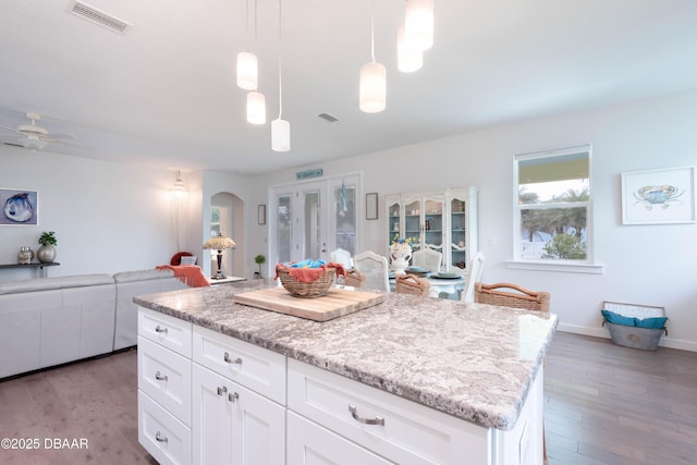 kitchen with light wood-type flooring, a kitchen island, white cabinets, and hanging light fixtures