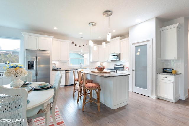 kitchen featuring appliances with stainless steel finishes, light wood-type flooring, pendant lighting, a kitchen island, and white cabinets