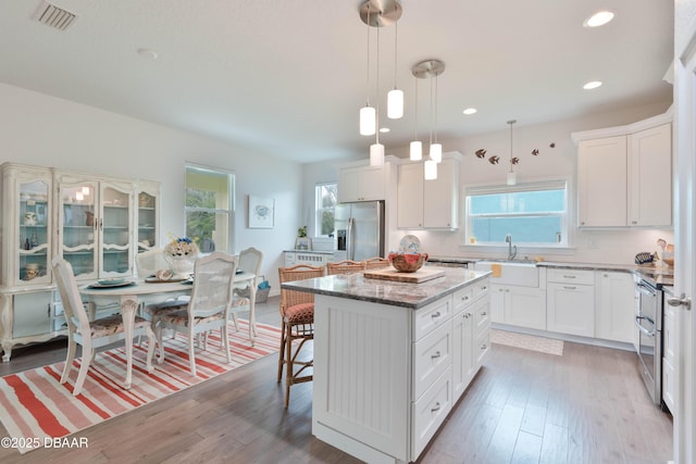 kitchen featuring a center island, white cabinetry, stainless steel appliances, and decorative light fixtures